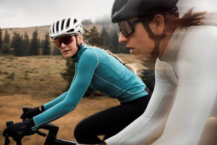 Ženska in moški kolesarita v termo kolesarskih oblačilih, v ozadju pokrajina.